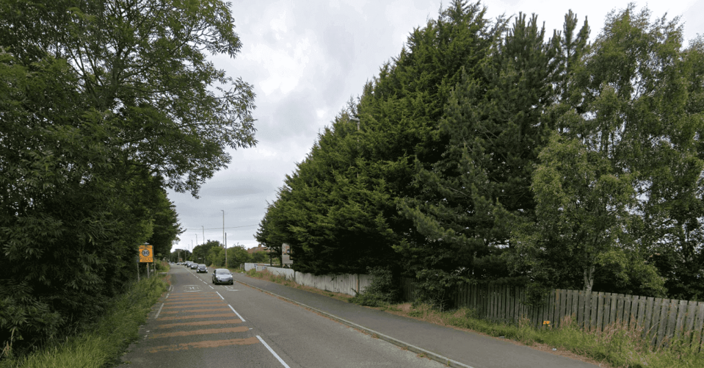 A two-lane road bordered by tall trees and a wooden fence, with cars driving and a speed limit sign on the left, evokes the charm of scenic carriageways while ensuring travellers comply with section 154 regulations.
