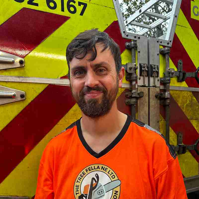 Man with orange top smiling at camera in front of a red and yellow striped van